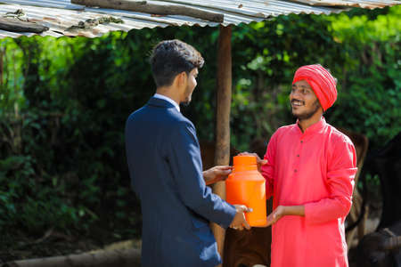 Indian farmer and animal husbandry officer holding milk bottle at dairy farmの写真素材