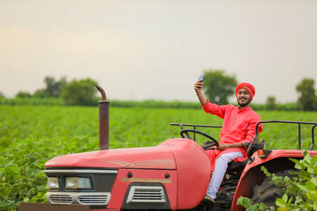 Indian farmer working with tractor and Using smartphone at fieldの写真素材
