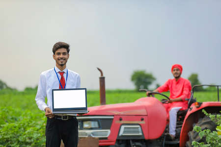 Farmer sitting on tractor and Young indian bank officer using laptop at agriculture fieldの写真素材