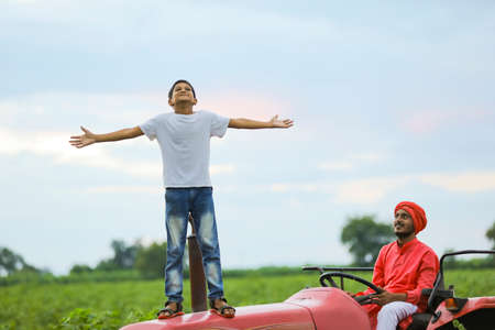 Indian farmer and cute little child enjoying tractor ride in agriculture fieldの写真素材