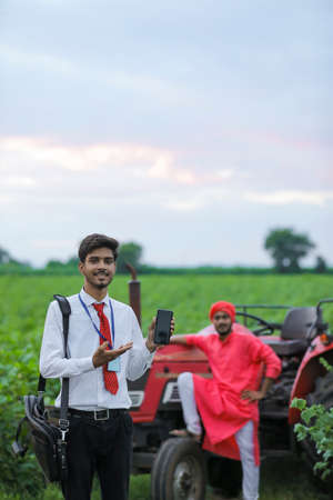 Young indian bank officer showing mobile screen at agri fieldの写真素材