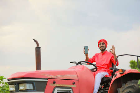 Indian farmer sitting on tractor and showing blank mobile screenの写真素材