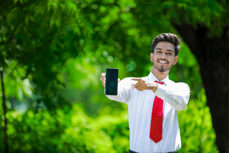 Copy space on his smart phone.Confident young Indian man showing his smart phoneの写真素材