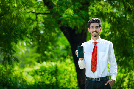 Copy space on his smart phone.Confident young Indian man showing his smart phoneの写真素材