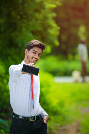 Copy space on his smart phone.Confident young Indian man showing his smart phoneの写真素材