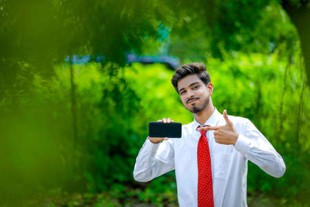 Copy space on his smart phone.Confident young Indian man showing his smart phoneの写真素材
