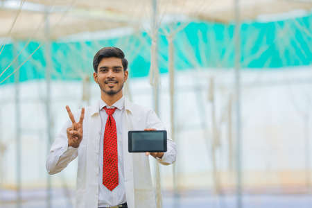 Technology and people concept, Young indian agronomist showing tablet or smartphone at greenhouseの写真素材