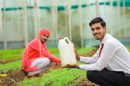 Young indian agronomist and farmer showing bottle at greenhouseの写真素材