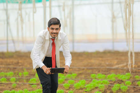 Technology and people concept, Young indian agronomist using tablet at greenhouseの写真素材