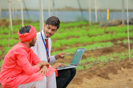Young indian agronomist showing some information to farmer in laptop at greenhouseの写真素材