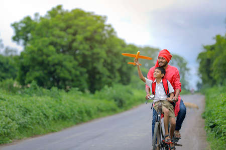 dreams of flight! indian child playing with toy airplane with his father on cycle