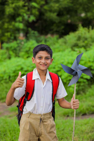 Cute indian child holding school bag and playing with pinwheel on road side