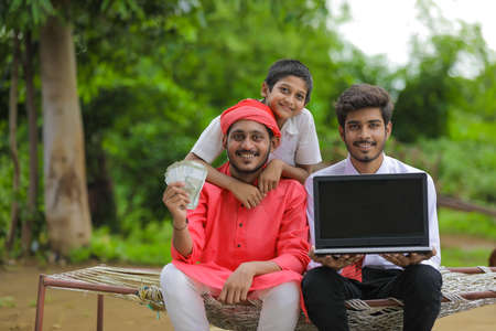 Young indian farmer showing indian rupees with bank officer at homeの写真素材