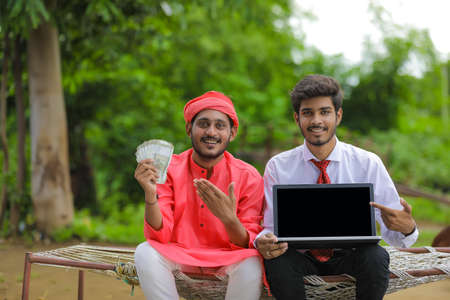 Young indian farmer showing indian rupees with bank officer at homeの写真素材