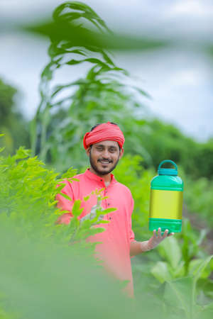 Young indian farmer showing fertilizer bottle at green fieldの写真素材