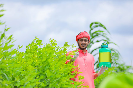 Young indian farmer showing fertilizer bottle at green fieldの写真素材