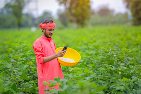 Young indian farmer using smartphone in green cotton field