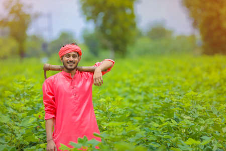 Young indian farmer holding farm equipment in hand at cotton field