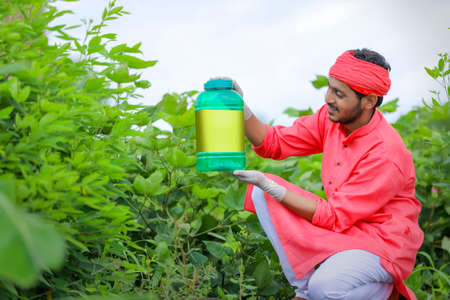 Young indian farmer showing fertilizer bottle at green field