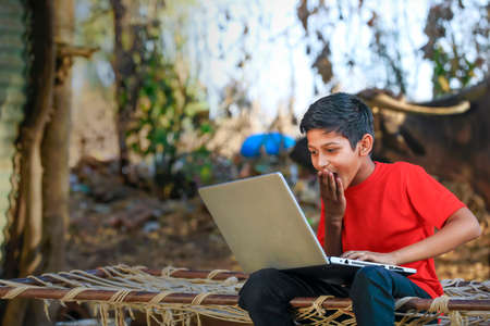 Cute little Indian/Asian boy studying or playing game with laptop computerの写真素材