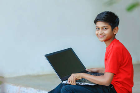 Cute little Indian/Asian boy studying or playing game with laptop computerの写真素材