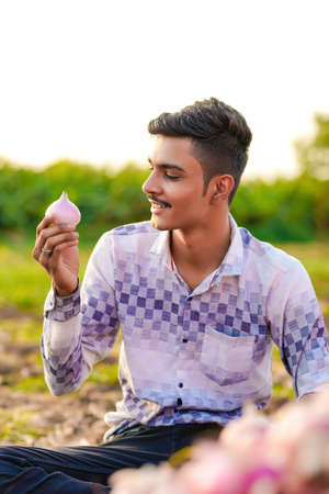 Young Indian farmer holding an onion in hand at agriculture field