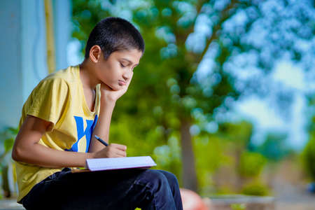 Indian school boy holding phone distance learning class using mobile application, watching online lesson, video calling in app making notes studying at homeの写真素材