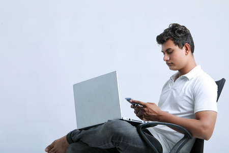 young indian man working on laptop and using smartphone.
