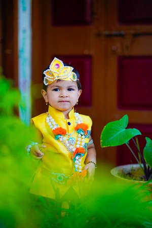 happy Janmashtami Greeting Card showing Little Indian boy posing as Shri krishna or kanha/kanhaiya with Dahi Handi picture and colourful flowers.の写真素材