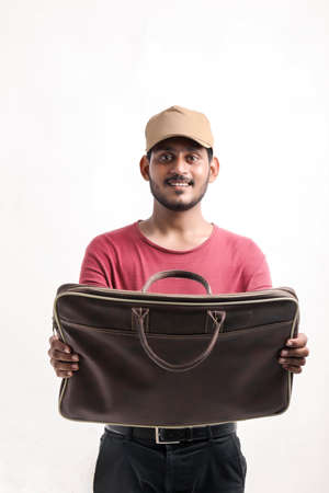 Portrait of a excited happy young delivery man in cap standing over white background and holding bag...