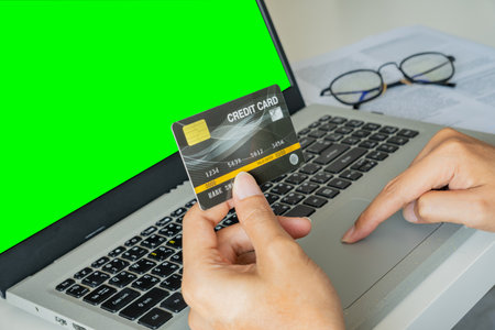 A person holds a credit card while browsing on a green-screen laptopâ€”signaling online...