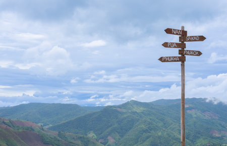 At the edge of a lush mountain vista, a weathered signpost points toward Nan, Pua, Phukha, and...