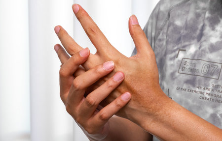 Man pressing aching palm with thumb, visible muscle tension and tendon strain in a bright clinical environment. Ideal for palm pain relief, hand therapy, and tendon injury ads.の写真素材
