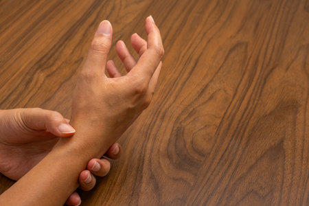 Work-induced wrist pain, hand gripping wrist on wooden desk. Highlights repetitive strain, tendon stress, or early signs of carpal tunnel syndrome.の写真素材