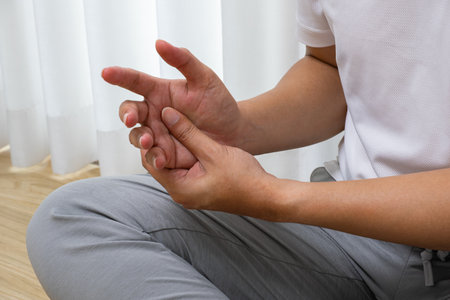 Morning hand painâAsian man massages fingers post-workout. Early joint strain in serene indoor setting, ideal for orthopedic or rehab ads.の写真素材