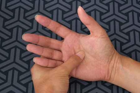 Close-up of hand pressing palm to relieve post-work pain. Medical concept for muscle, nerve, and orthopedic care in workplace-related hand strain.の写真素材