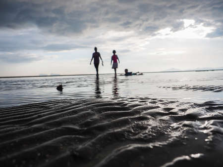 Silhouette of family on the sandy beach at sunset and cloudy skyの写真素材