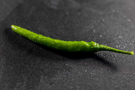 Green chili with drops of water and natural light on black tableの写真素材