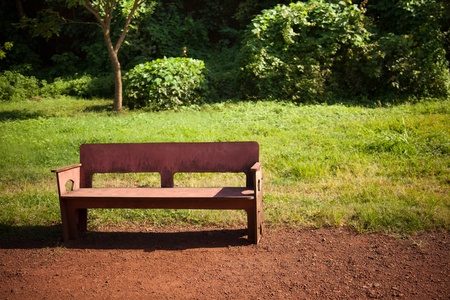 cemented  bench in park having green grass and red soil in sunlightの写真素材