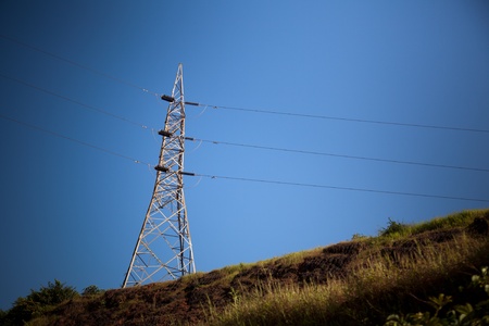 Electricity pylon with grid power under blue sky on hill の写真素材