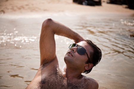 Indian Happy young man getting out of the water with sunglassesの写真素材