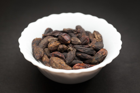 Organic Chebulic Myrobalan or Choti Harad Terminalia chebula in white ceramic bowl on dark...