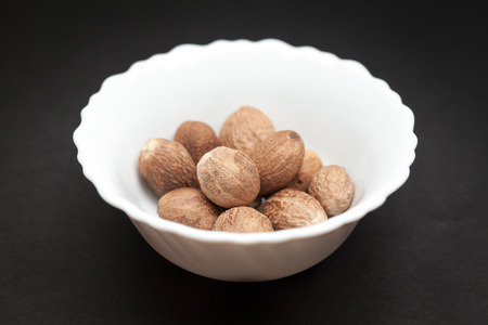 Organic Nutmeg Seed or Jaiphal Myristica fragrans in white ceramic bowl on dark background.の写真素材