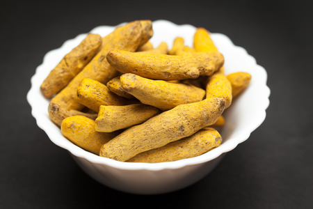 Organic Long Turmeric or Haldi Curcuma longa in white ceramic bowl on dark background.
