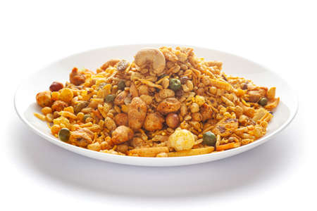 Pile of Indian spicy snacks (Namkeen) - 'All in one' in a white plate, made with fried peanut, corn flakes, sweet pea, pulses, cashew nuts, etc. side view, against the white background.の写真素材