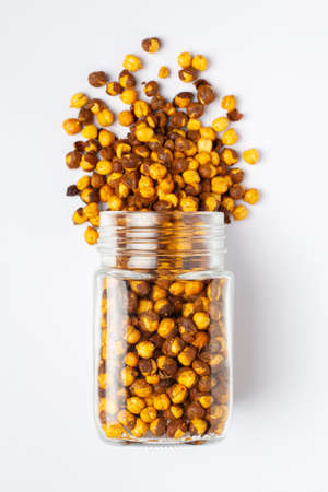 Crunchy Roasted Chana Masala spilled out and in a glass jar, made with Bengal Grams or Chickpeas. Indian spicy snacks (Namkeen),  Top view, over the white background.の写真素材