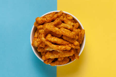 Close up of tangy Potato Puff Snacks sticks, Popular Ready to eat crunchy and puffed snacks sticks tangy spicy  orange color over yellow backgroundの写真素材