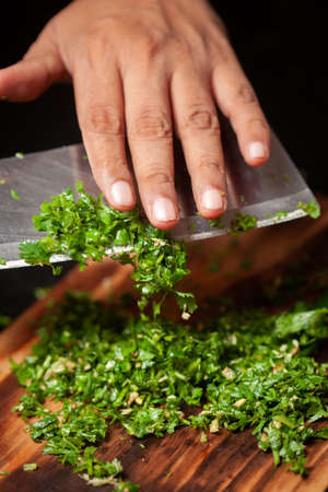 Close-up of hands chopping fresh green coriander or parsley leaves on a wooden cutting board.の写真素材