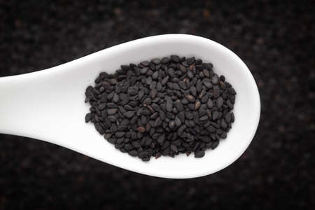 Macro Close up of Organic Black Sesame seeds(Sesamum indicum) or Black Til with the shell on a white ceramic soup spoon in a blurred background. Top viewの写真素材