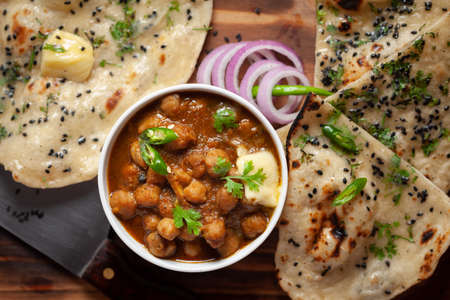 Close-up of fresh, hot tandoori roti or butter naan garnished with black till and green fresh coriander leaves and chole. A typical, traditional north indian panjabi food.の写真素材